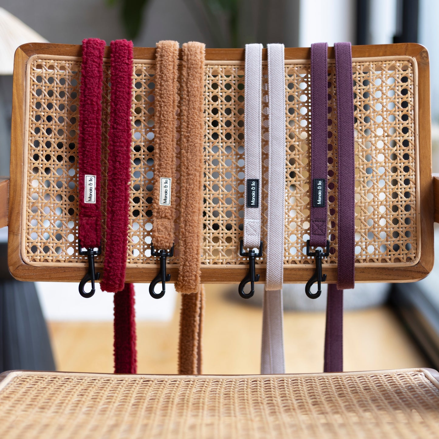 Four leads dark red, beige, light brown and purple hang with fixed length over a woven chair. Crafted from quality materials, these leads are displayed indoors under natural light, highlighting their elegance and style.