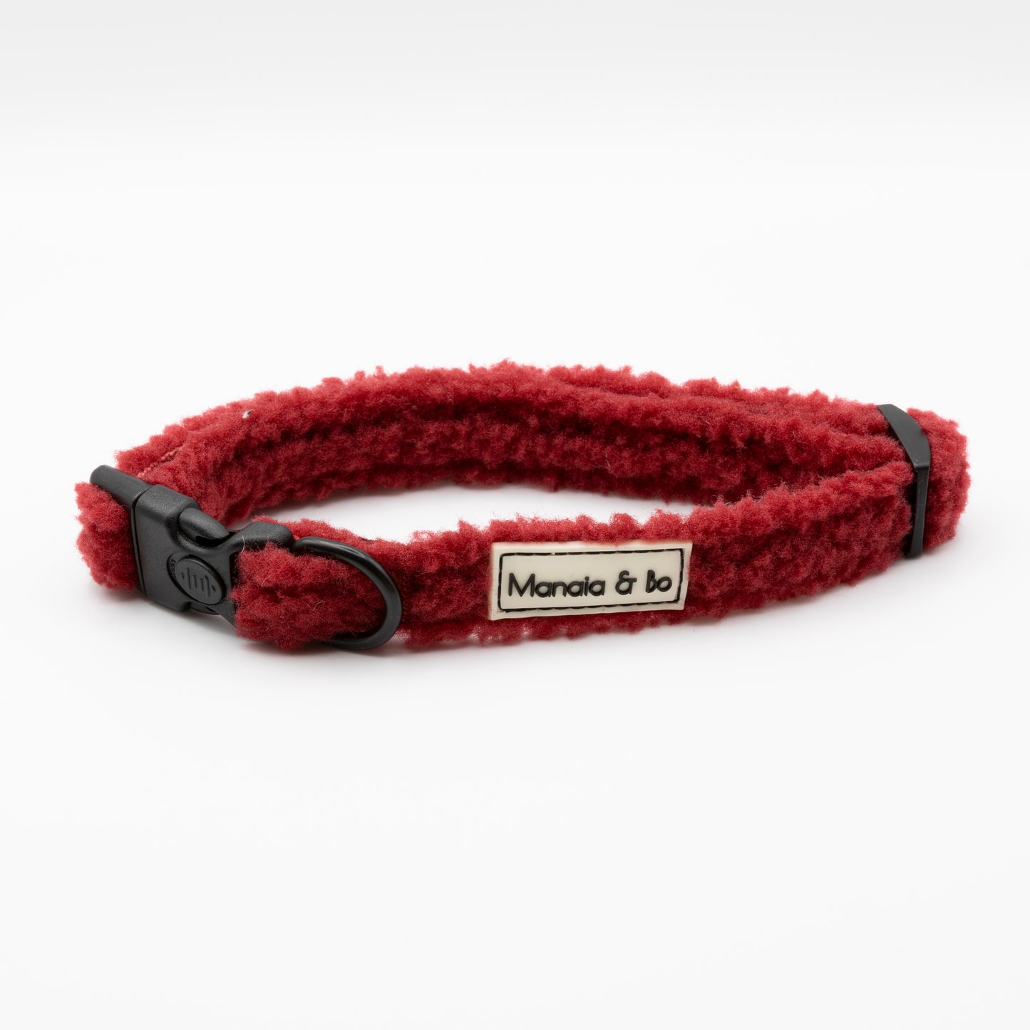 The Bordeaux Teddy Dog Collar is a red, fluffy, soft collar with adjustable black plastic hardware and a "Manala & bo" label on a white background.