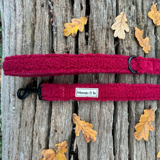Bordeaux (burgundy) teddy material dog lead laying on a tree trunk from top showing both ends. Comfortable material with black metal d-ring by the lead handle and black metal swivel snap hook.