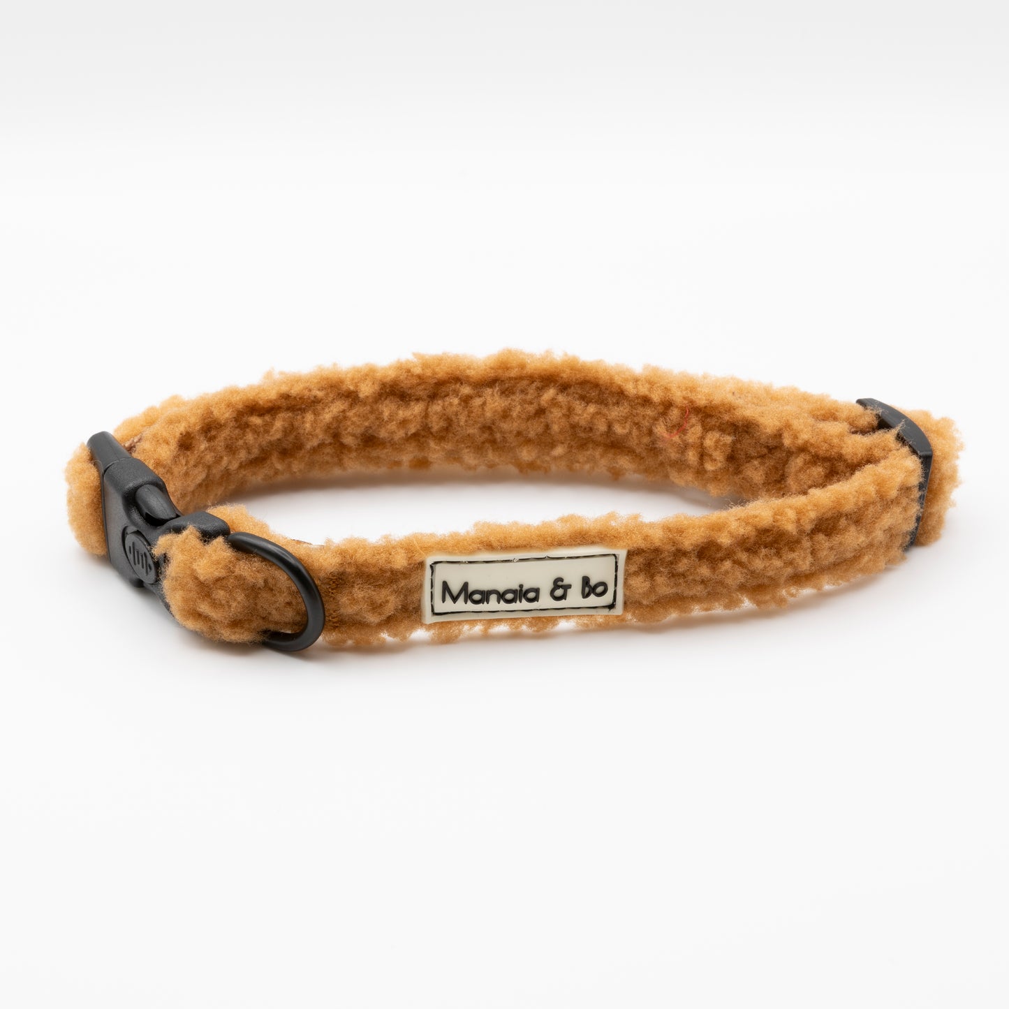 The Caramel Teddy Dog Collar is a tan, fluffy adjustable collar with black plastic buckles and a "Mancia & bo" label, shown on a white background.