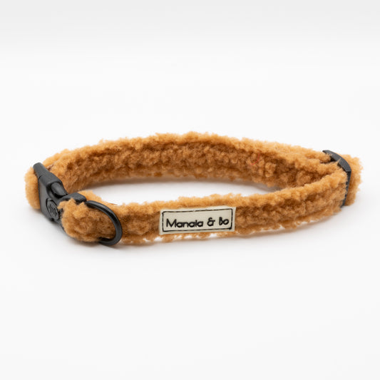 The Caramel Teddy Dog Collar is a tan, fluffy adjustable collar with black plastic buckles and a "Mancia & bo" label, shown on a white background.