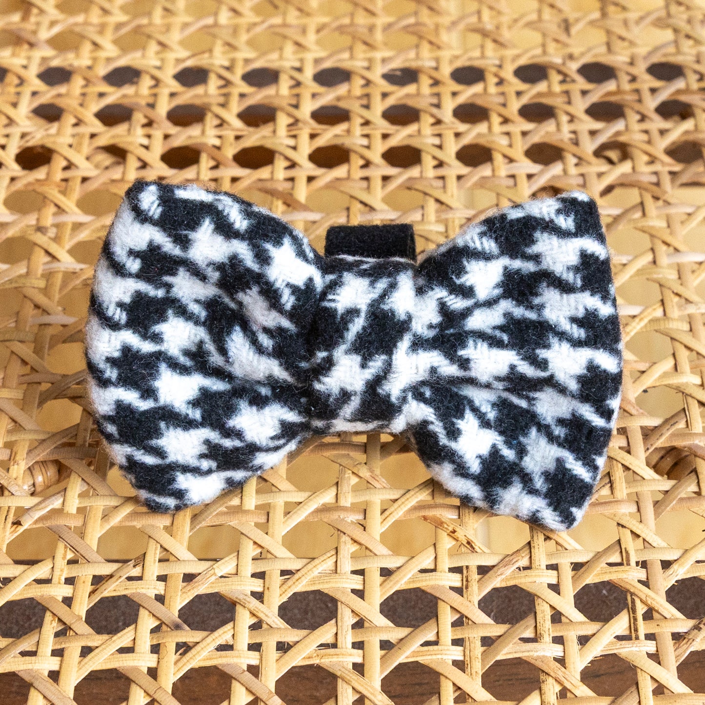 The Classic Houndstooth Dog Bow Tie, shown on a woven rattan surface, is a stylish black and white accessory that’s perfect for any dog’s collection.
