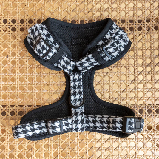 The Classic Houndstooth Harness, Lead & Collar set in black and white tweed with adjustable straps is displayed on woven rattan, offering a timeless look for your dog.