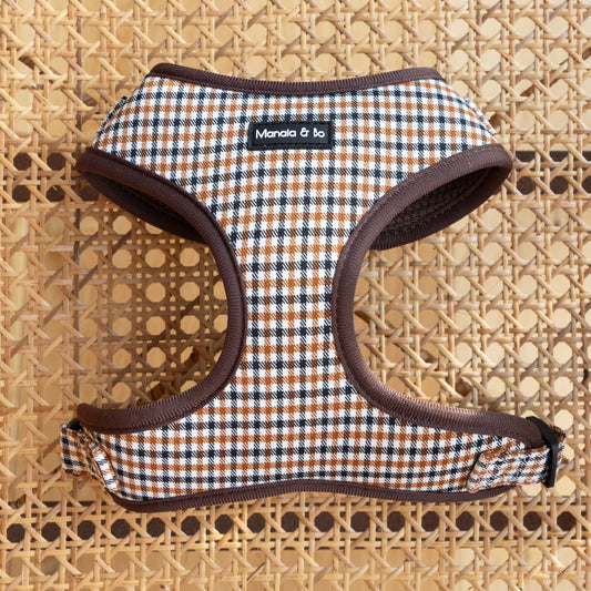 The Cocoa Heritage Lite Dog Harness, a small adjustable brown and white plaid design with a Manala & Bo label, is shown on a woven rattan surface.