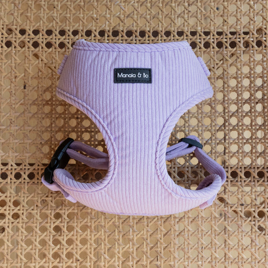 The Lavender Cord Harness, a textured pink adjustable dog harness with a black plastic fastenings and metal d-ring rests on a woven rattan surface symbolising the high-quality pet accessories line.