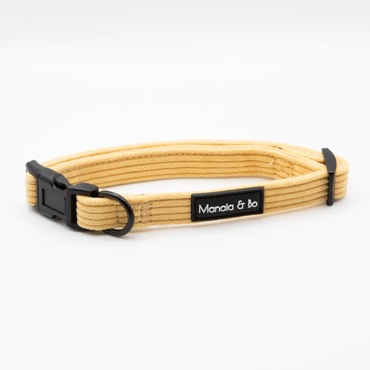 The Mellow Cord Dog Collar is a beige ribbed cord collar for pets featuring a black plastic buckle, adjustable slider, and a black Manala & bo tag. Shown on a plain white background.