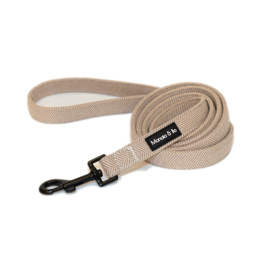 The Nougat Tweed Dog Lead is a beige leash with a black metal clip, showcasing a herringbone pattern. It combines elegance and style with quality craftsmanship.