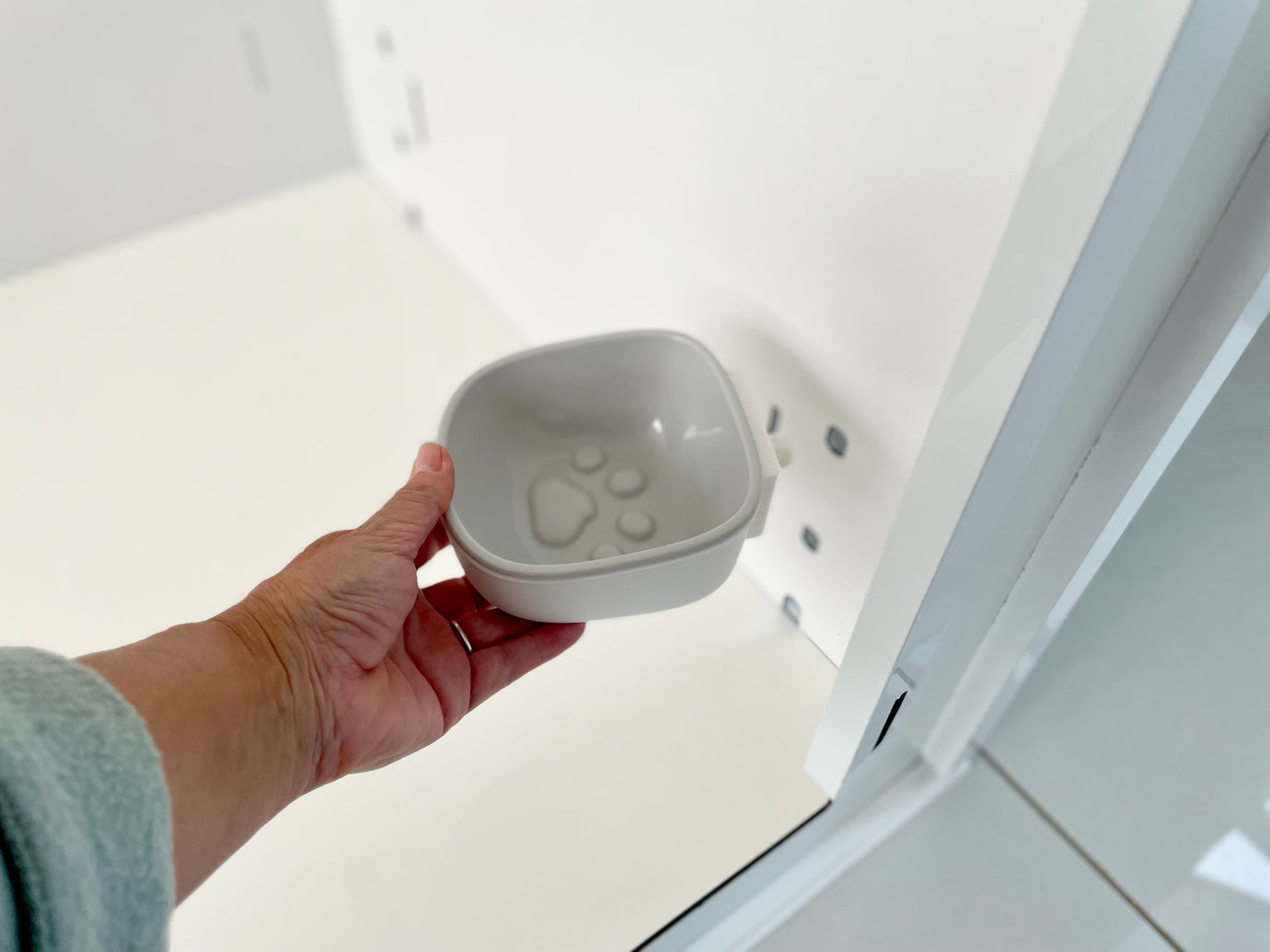 A hand holds a small white pet bowl with a paw print, next to the Petpen Crate—a minimalist, stylish solution for crate training your pet.