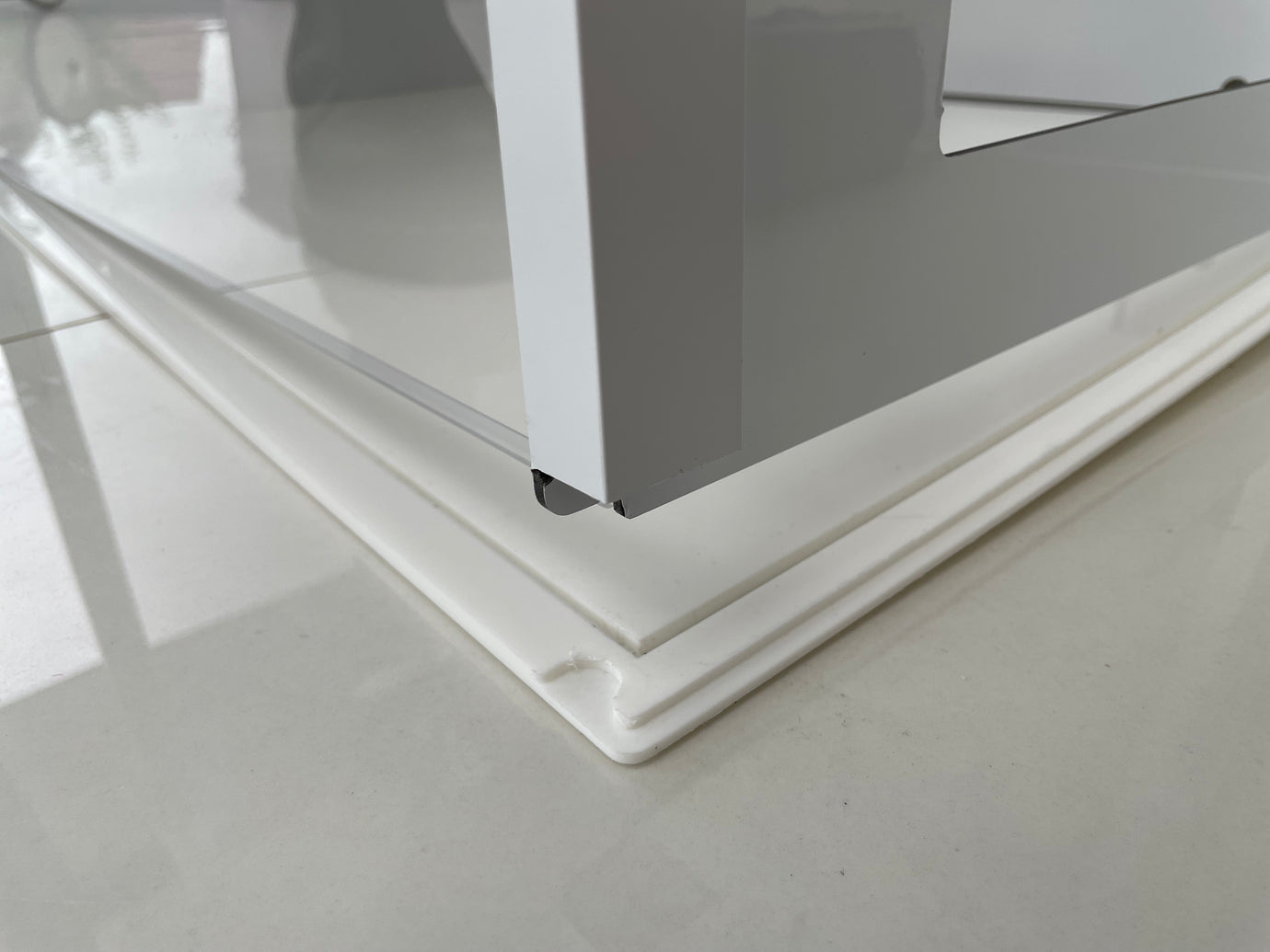 Close-up of the Petpen Crate’s white metal frame on glossy white tiles, resting on a raised white base with a beveled edge and corner notch—perfect for stylish crate training or use as a modern pet den.