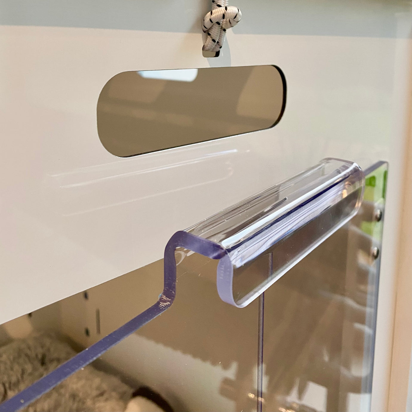 Close-up of the Petpen Crate’s clear acrylic handle on its glass door, with a rectangular cutout above the handle and a knotted rope above the cutout in a white minimalist design.