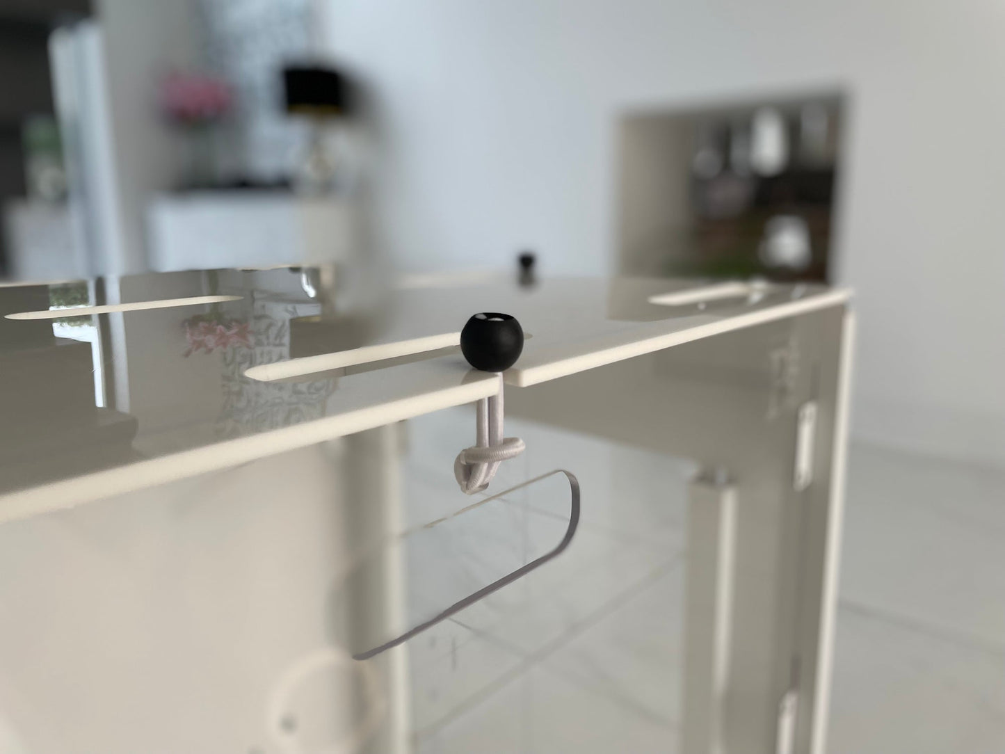 A close-up of the Petpen Crate, a white modern pet den with a clear acrylic door and black knob latch, set in a bright, minimalist room with blurred background furnishings.