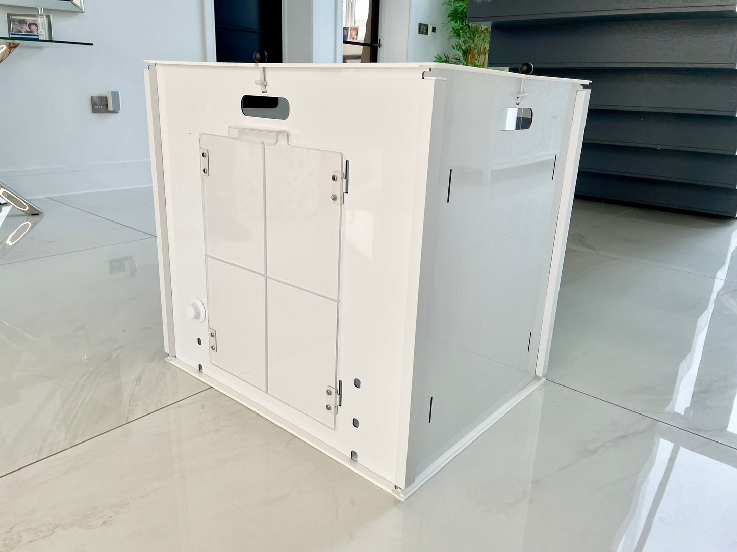 The Petpen Crate, a white minimalist pet crate with a clear door and ventilation holes, sits on glossy tiles in a bright modern room—an ideal, stylish den for crate training your pet.