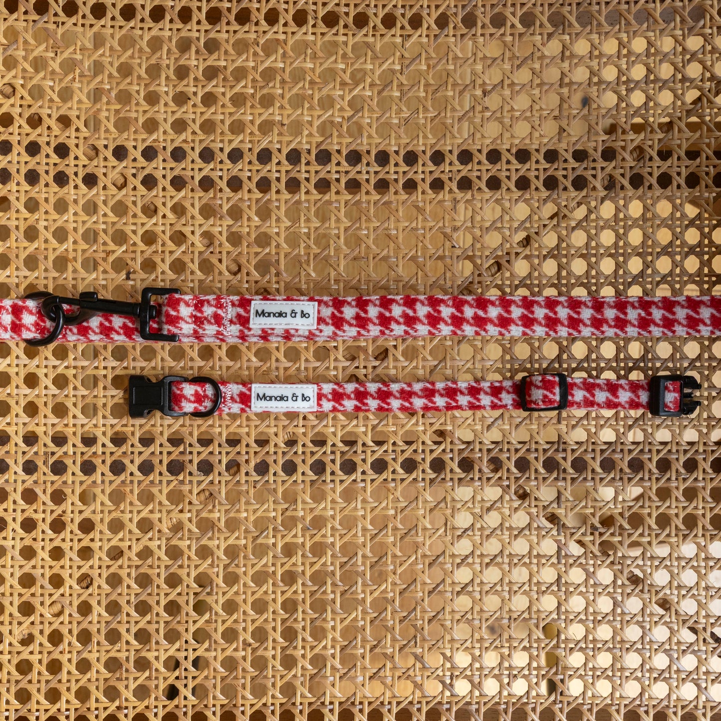 Two Scarlet Houndstooth Collar & Lead sets with black buckles and Monada & Fa labels are displayed on a woven rattan surface. Each adjustable dog collar offers stylish comfort for your pup.