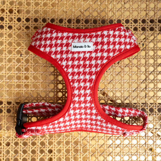 The Scarlet Houndstooth Dog Harness, with red and white tweed and red trim by Manola & Co, rests on a woven rattan surface. This adjustable harness offers stylish comfort for your dog.