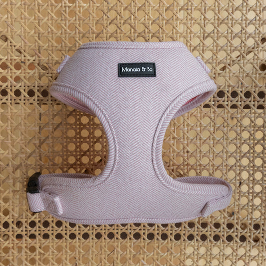 The Tea Rose Tweed Dog Harness, featuring an adjustable pink herringbone pattern, rests on a woven rattan surface. The beautiful design offers both style and comfort for your pampered pooch