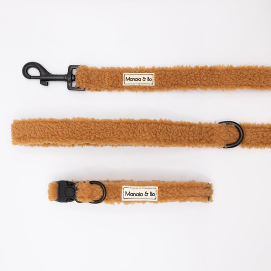 The Caramel Teddy Collar & Lead set features brown faux-shearling, black hardware, a Manola & Bo label, an adjustable collar with lockable buckle, and matching leash—displayed on a white background.