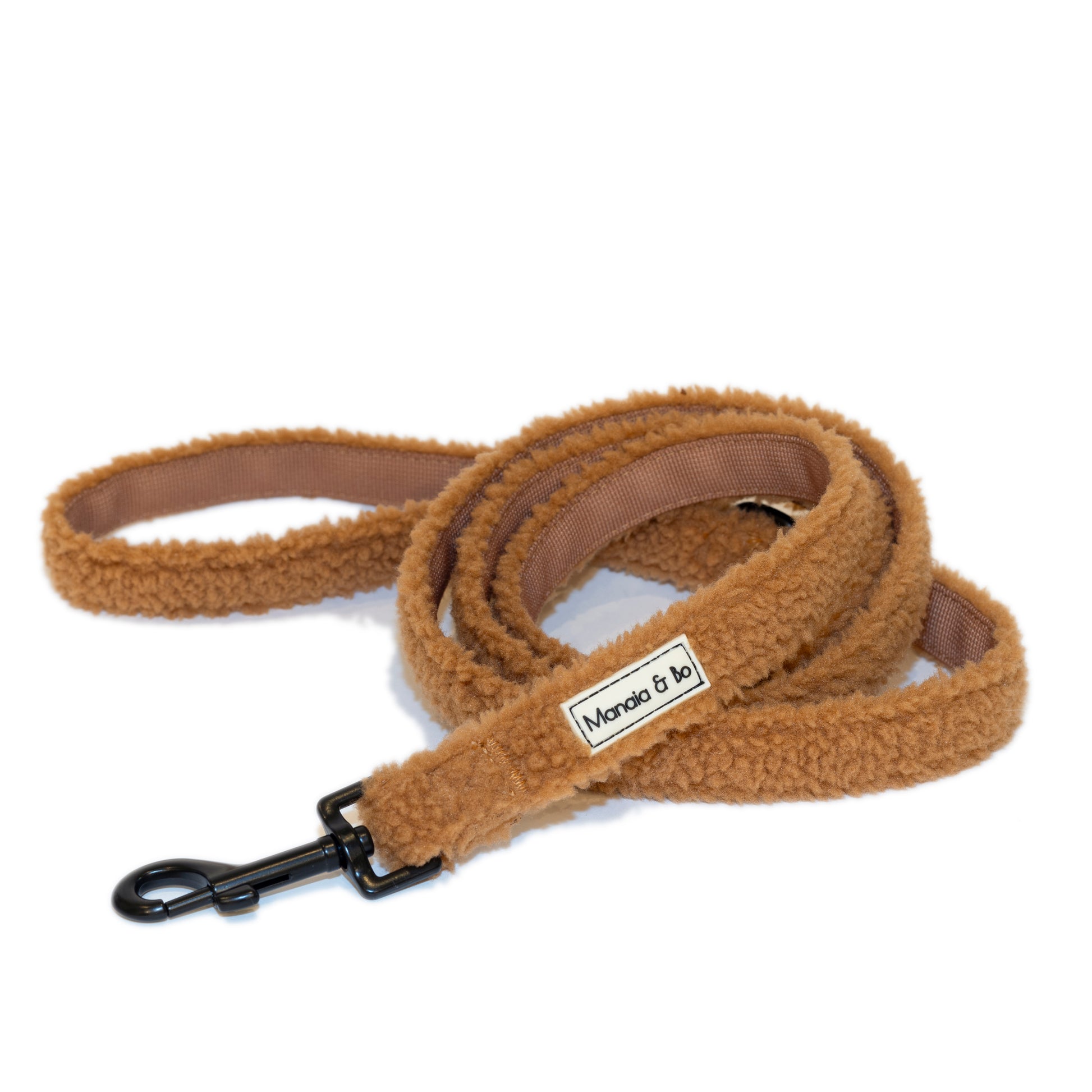 The Caramel Teddy Dog Lead is a coiled, fluffy brown leash made from quality materials, featuring a black metal clip, capturing the essence of a stylish dog lead. The item is displayed on a white background.