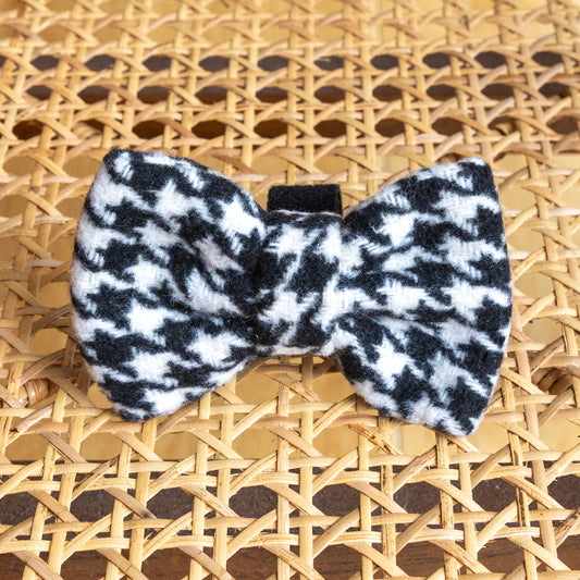 The Classic Houndstooth Dog Bow Tie, shown on a woven rattan surface, is a stylish black and white accessory that’s perfect for any dog’s collection.