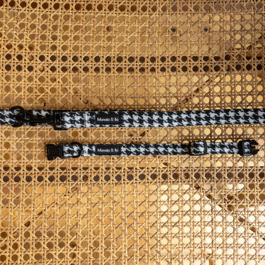 Two Classic Houndstooth Collar & Lead sets with black hardware are displayed on a woven cane surface. Each adjustable collar features a small “Monada & Co.” label.