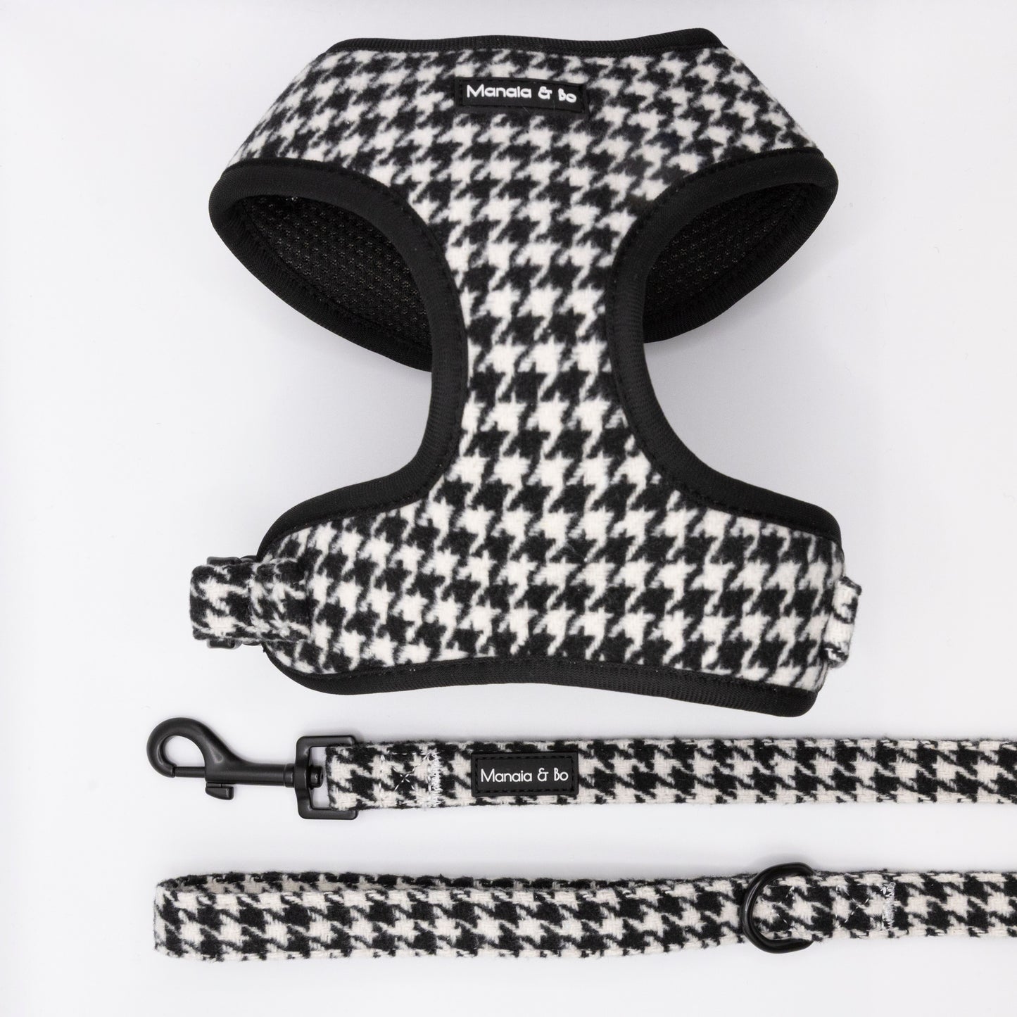 The Classic Houndstooth Harness & Lead set, shown in black and white houndstooth with a “Moncia & To” label, is displayed on a white background. This adjustable duo offers both comfort and style for your pet.