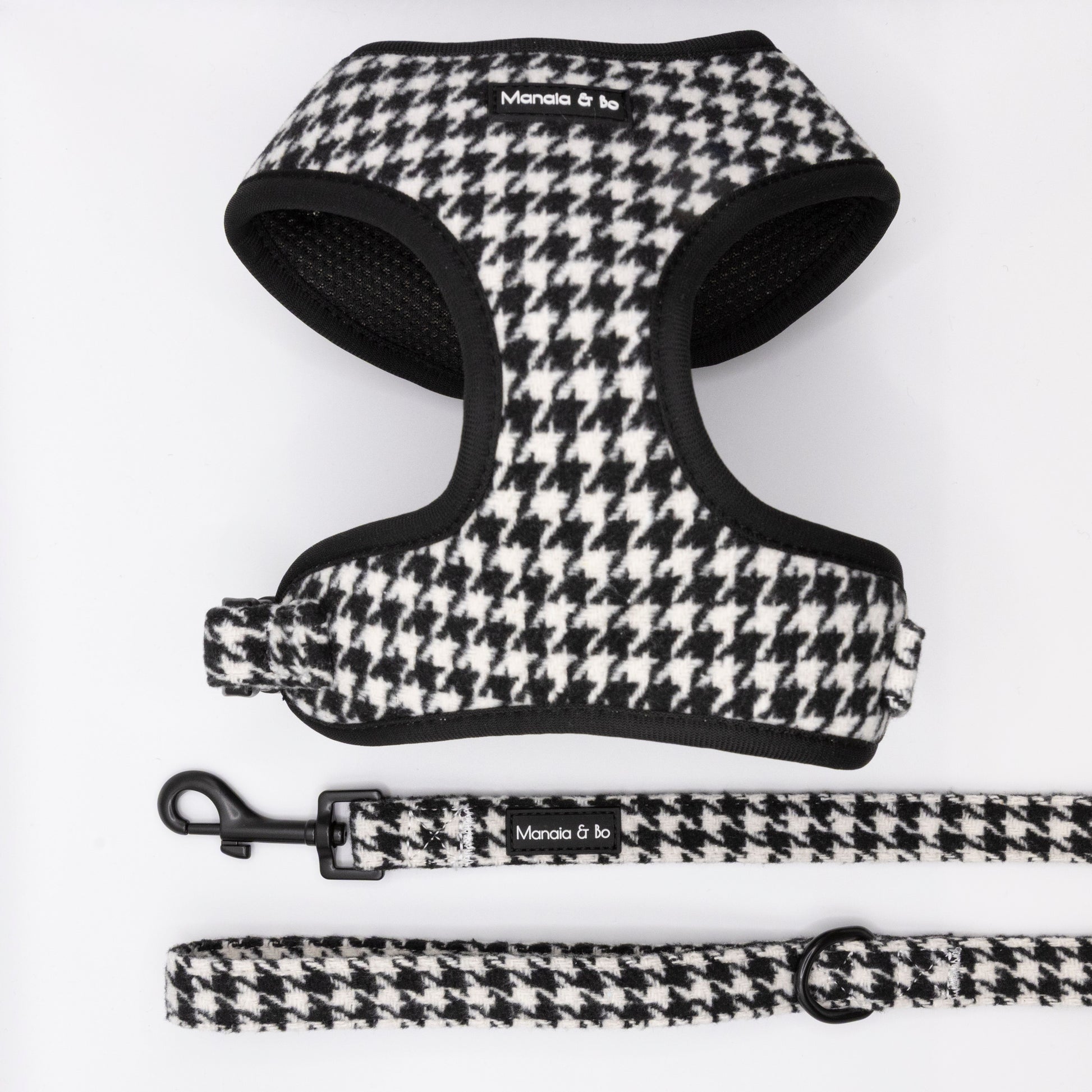 The Classic Houndstooth Harness & Lead set, shown in black and white houndstooth with a “Moncia & To” label, is displayed on a white background. This adjustable duo offers both comfort and style for your pet.