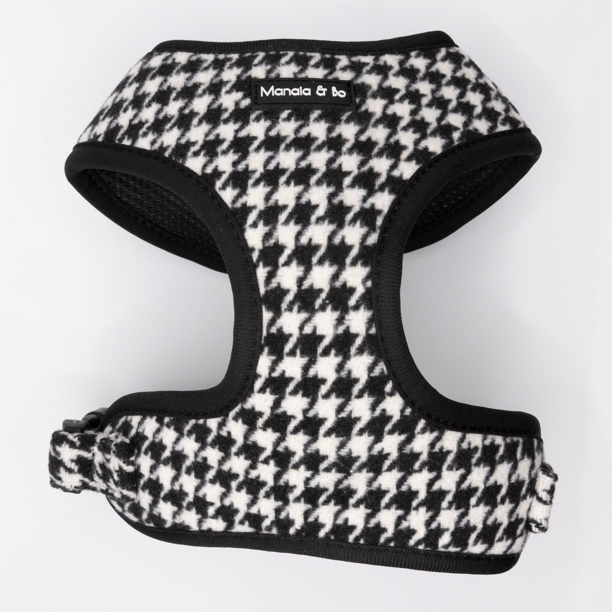 The Classic Houndstooth Dog Harness features a black and white houndstooth pattern with black trim and a "Manala & Bo" label on the front. This adjustable harness is displayed flat on a white background.