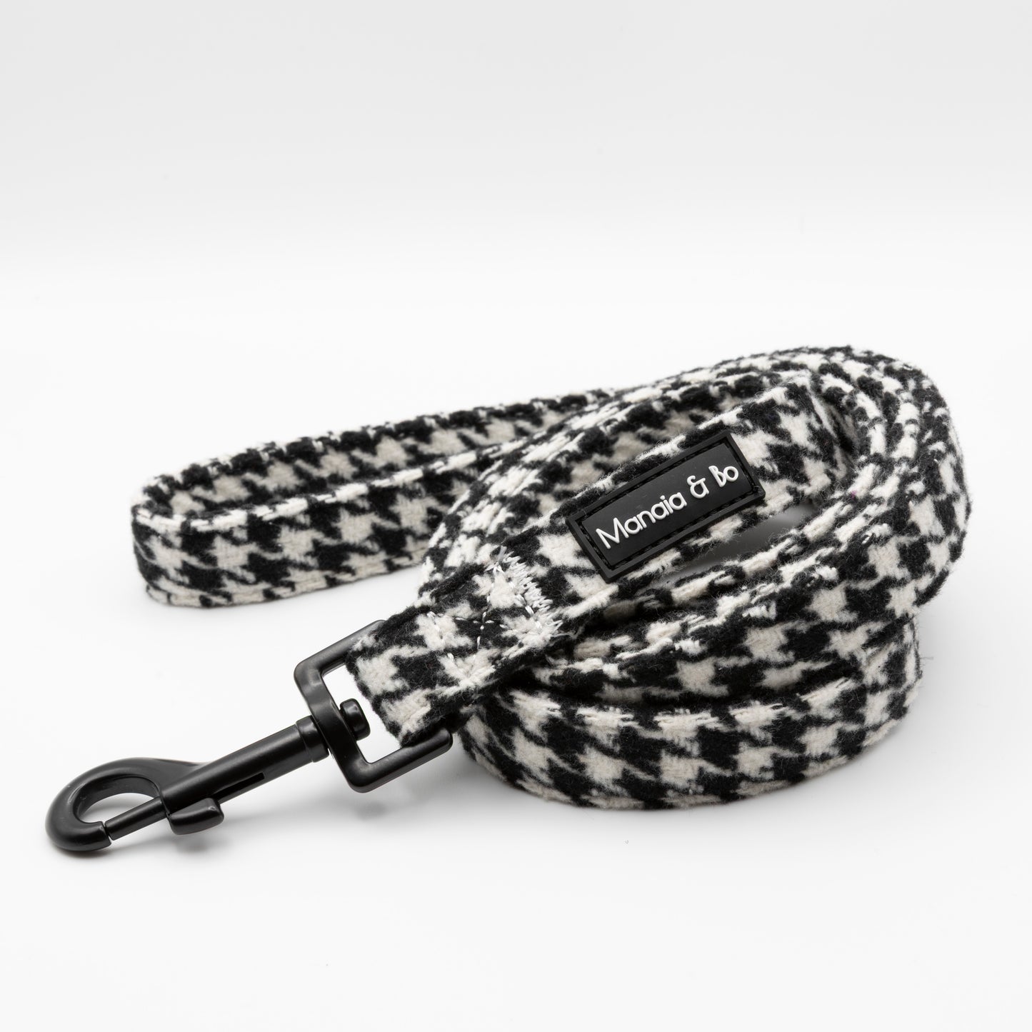 The Classic Houndstooth Dog Lead features black and white tweed, a sturdy black metal clasp, and a Mandia & bo label. Durable and stylish, it’s perfect for everyday walks. Pictured coiled neatly on a white background.