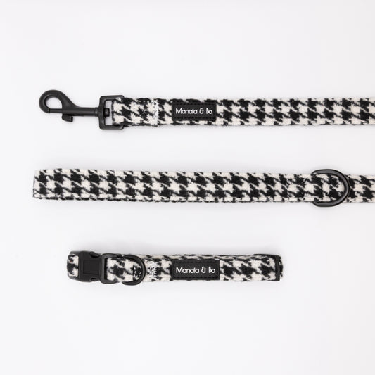 The Classic Houndstooth Collar & Lead, featuring a “Manola & bo” label, is shown on a white background. This adjustable collar offers classic black and white style with comfort for your pet and comes with a matching leash.