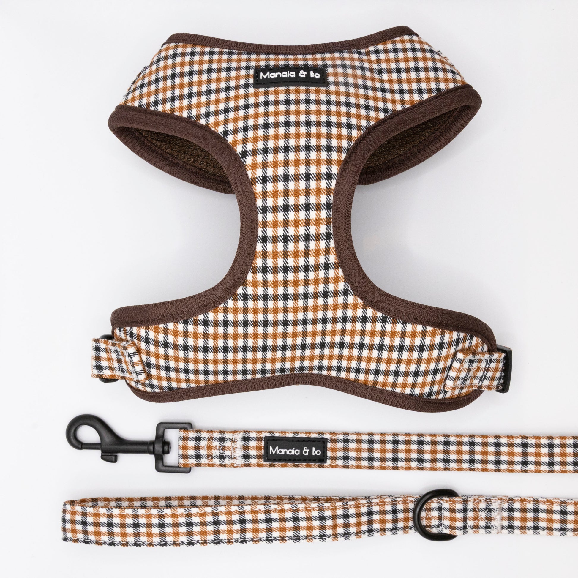 The Cocoa Heritage Lite Harness & Lead, featuring a brown, white, and tan plaid design, are displayed on a white background. The padded harness ensures comfort, and the matching leash comes with a sturdy black clasp. Both items are labeled Manala & Co.