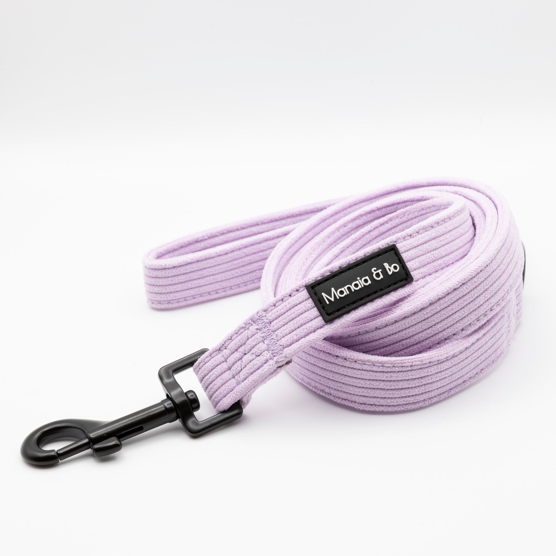 The Lavender Cord Dog Lead, a coiled lavender leash with a black metal clip and a Moncia & bo label, showcases stylish dog accessories on a white background.