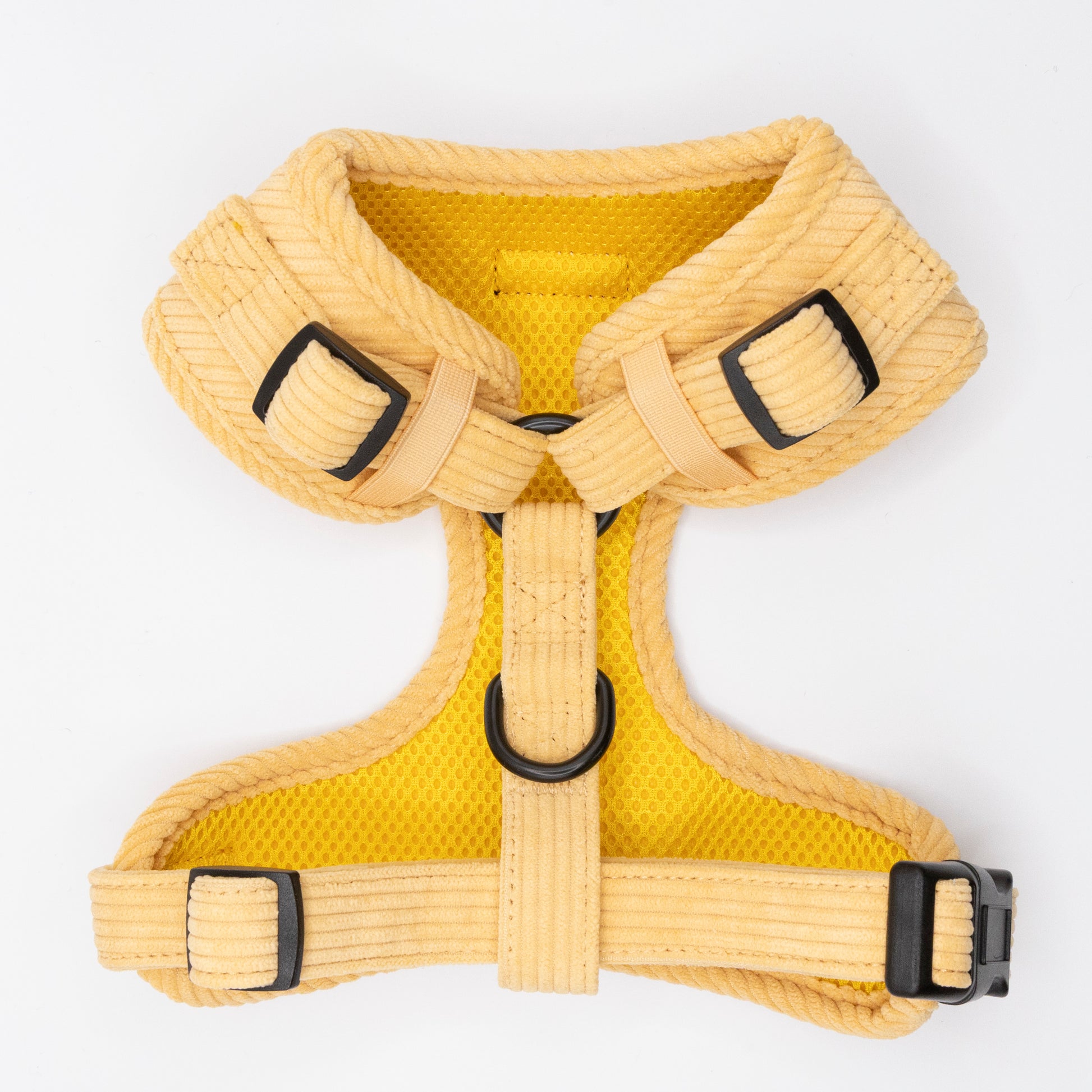 The Mellow Cord Dog Harness, yellow and padded for comfort, features adjustable straps, black buckles, a mesh lining, and a metal D-ring for secure leash attachment. Displayed flat on a white background.
