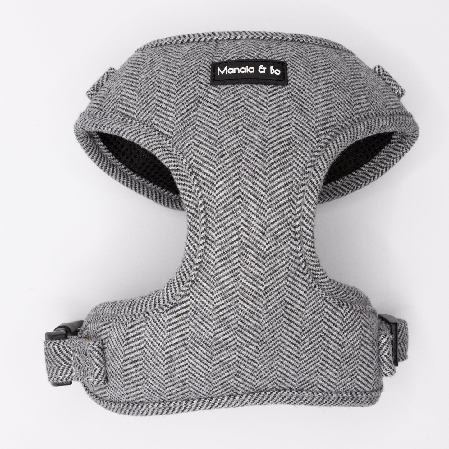 The Monochrome Tweed Harness & Lead features a gray herringbone pattern with black trim, adjustable straps, and "Manola & bo" label on the front. Ideal for small to medium dogs, it offers both comfort and support.