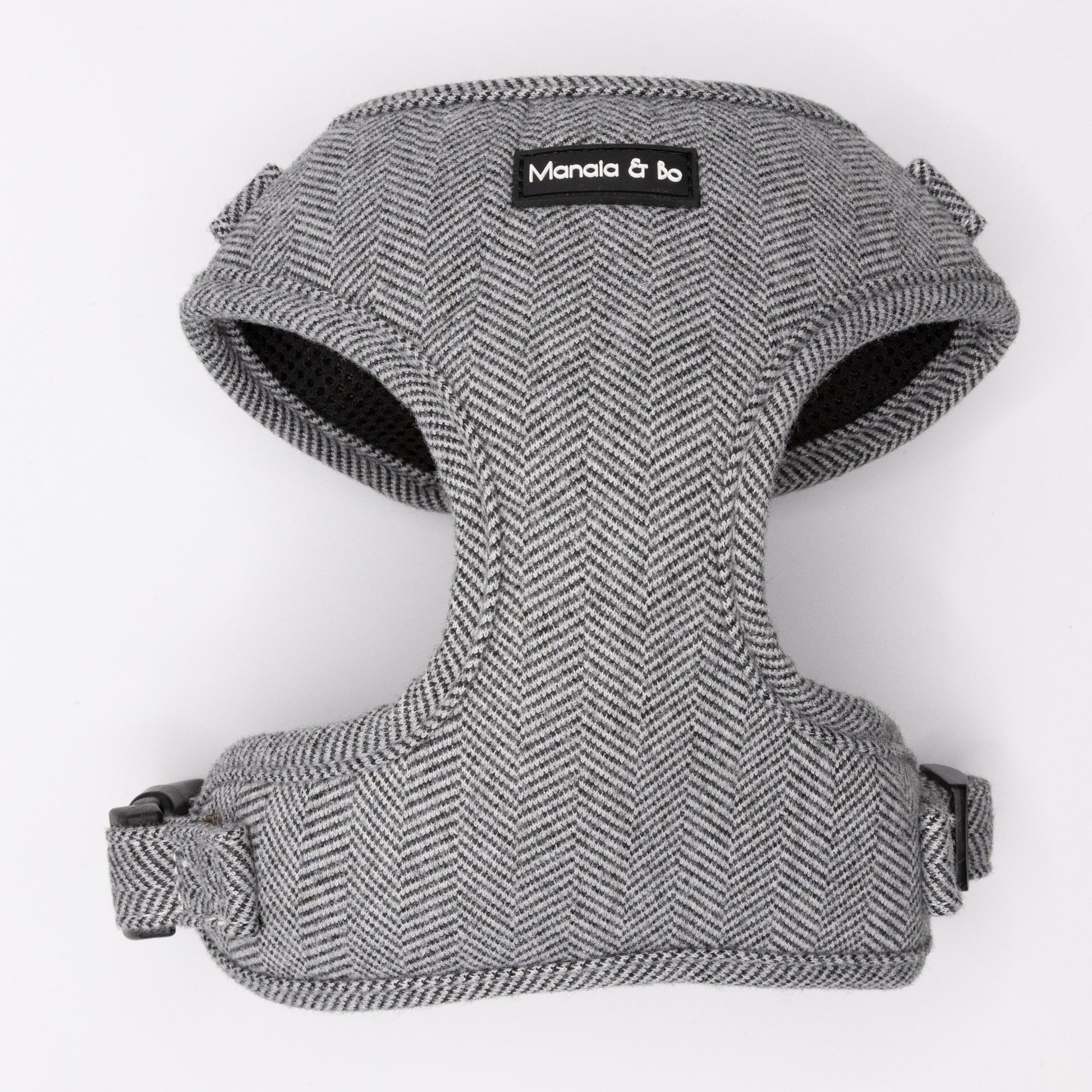 The Monochrome Tweed Harness & Lead features a gray herringbone pattern with black trim, adjustable straps, and "Manola & bo" label on the front. Ideal for small to medium dogs, it offers both comfort and support.