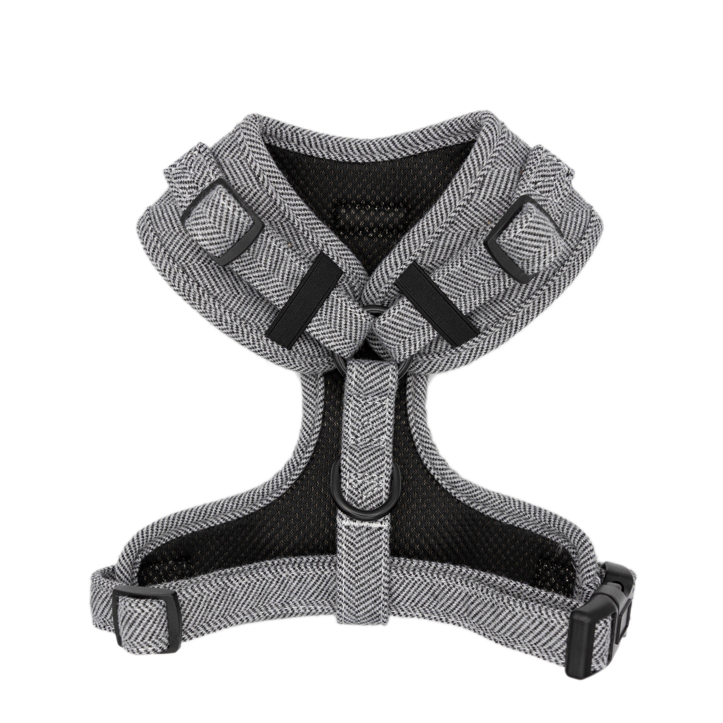 Monochrome (dark grey and white) adjustable dog harness on a white background from the back. Visible in the image is the black mesh lining and the tweed straps. along with the black plastic fastenings and black metal fixing ring for attaching a lead.