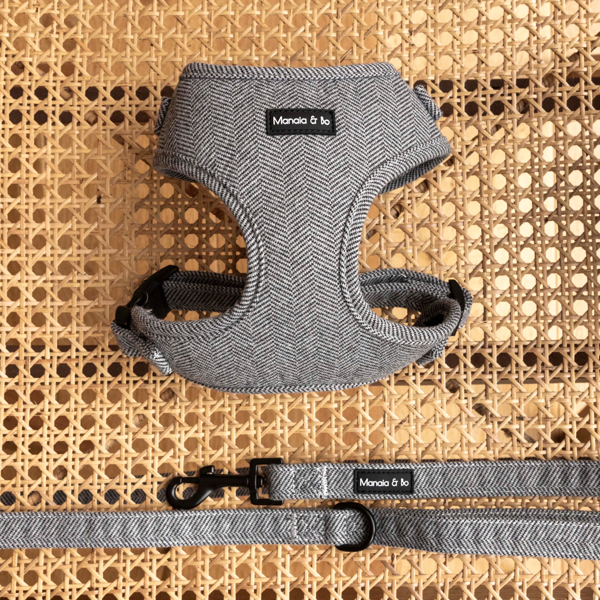 Gray herringbone dog harness and leash set displayed on a woven rattan surface. The set features black metal fastening for stress free walkies.