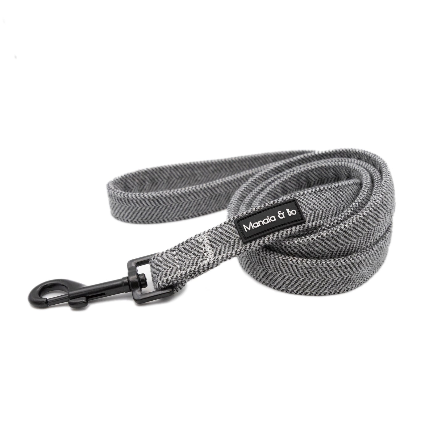 Monochrome (dark grey and white) tweed herringbone lead in a coil on a white background from the front. In the foreground is the black metal swivel snap hook.