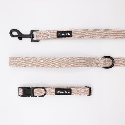 The Nougat Tweed Collar & Lead set features a beige herringbone-patterned collar and matching leash with black hardware, both labeled Mania & bo. The adjustable dog collar ensures a comfortable fit, all displayed on a white background.