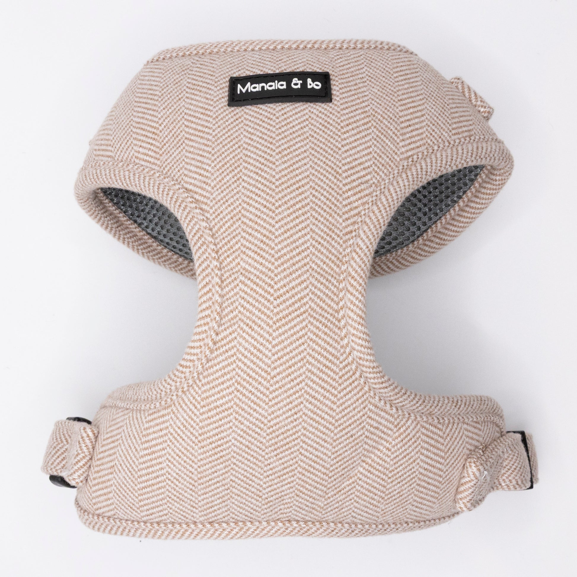 The Nougat Tweed Dog Harness, shown on a plain white background, is a beige herringbone fabric harness with adjustable straps and a black Manala & bo label on the front.