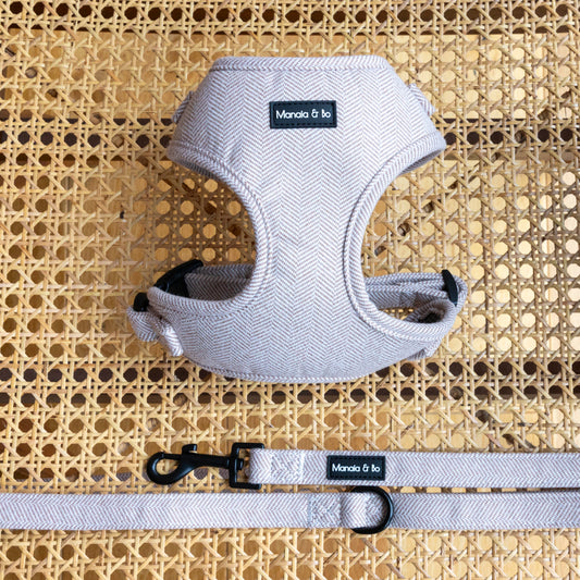 A Nougat dog harness and matching leash are displayed on a rattan chair. The leash has a black metal hook for securely fastening to a collar or harness.