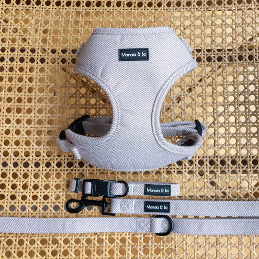 A Nougat Tweed Harness, Lead & Collar set with a beige herringbone pattern, rests on rattan. It features black metal hardware and a brand label. Made with quality pet materials, the adjustable harness ensures a perfect fit for any small to medium dog.