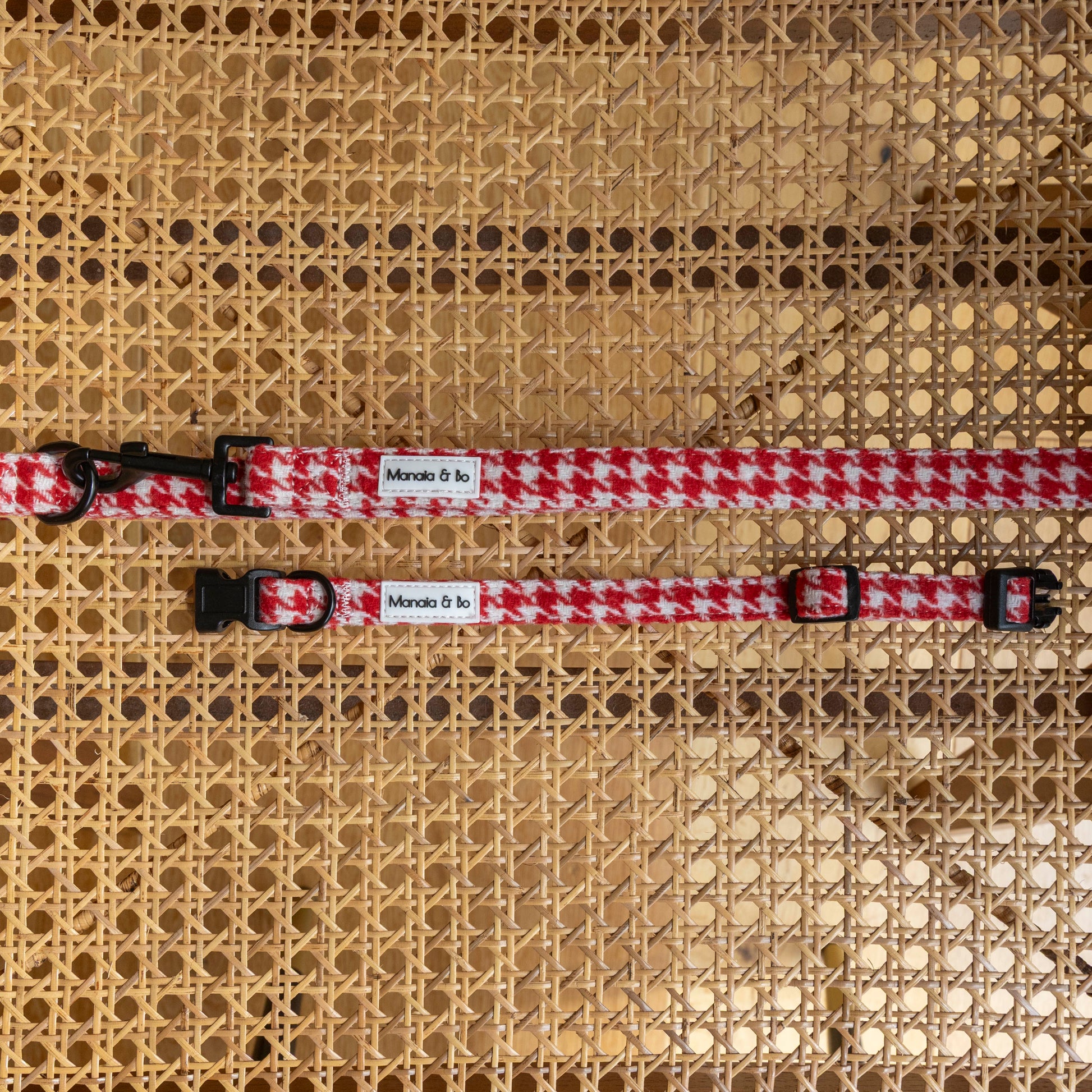 Two Scarlet Houndstooth Collar & Lead sets with black buckles and Monada & Fa labels are displayed on a woven rattan surface. Each adjustable dog collar offers stylish comfort for your pup.