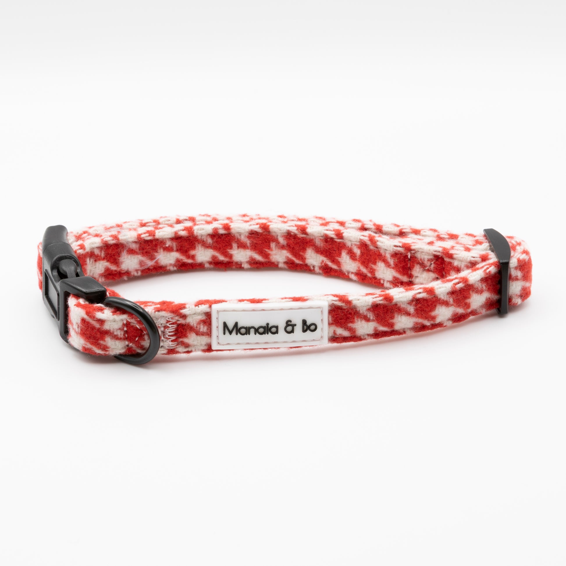 The Scarlet Houndstooth Dog Collar is red and white with a black plastic buckle, adjustable fit, and features a Manala & bo label on the side.