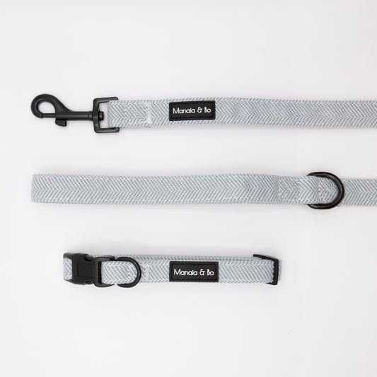 Sky Tweed Collar & Lead set in light gray with black metal hardware is displayed on a white background. Both feature a Mancia & bo label. The leash includes a clasp; the collar has a plastic buckle and metal ring.