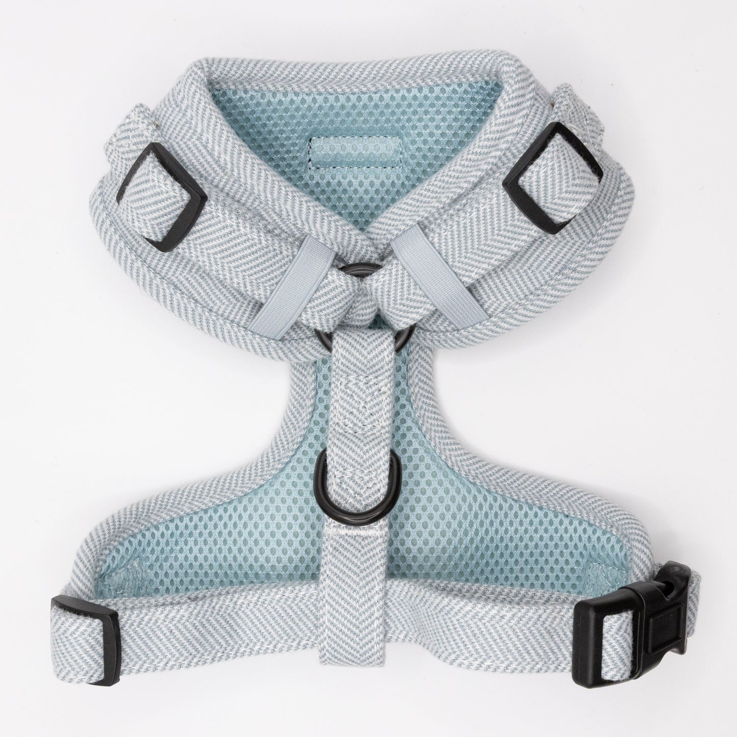 The Sky Tweed Dog Harness features a light blue and white herringbone pattern, black plastic buckles, and metal D-rings. Adjustable for a secure, comfortable fit on small to medium dogs. Shown laid flat on a white background.