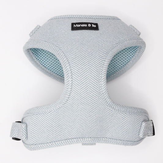 The Sky Tweed Dog Harness is a light gray herringbone tweed harness with a light blue mesh lining, adjustable straps, and a Manola & bo label on the front, designed for small to medium dogs.