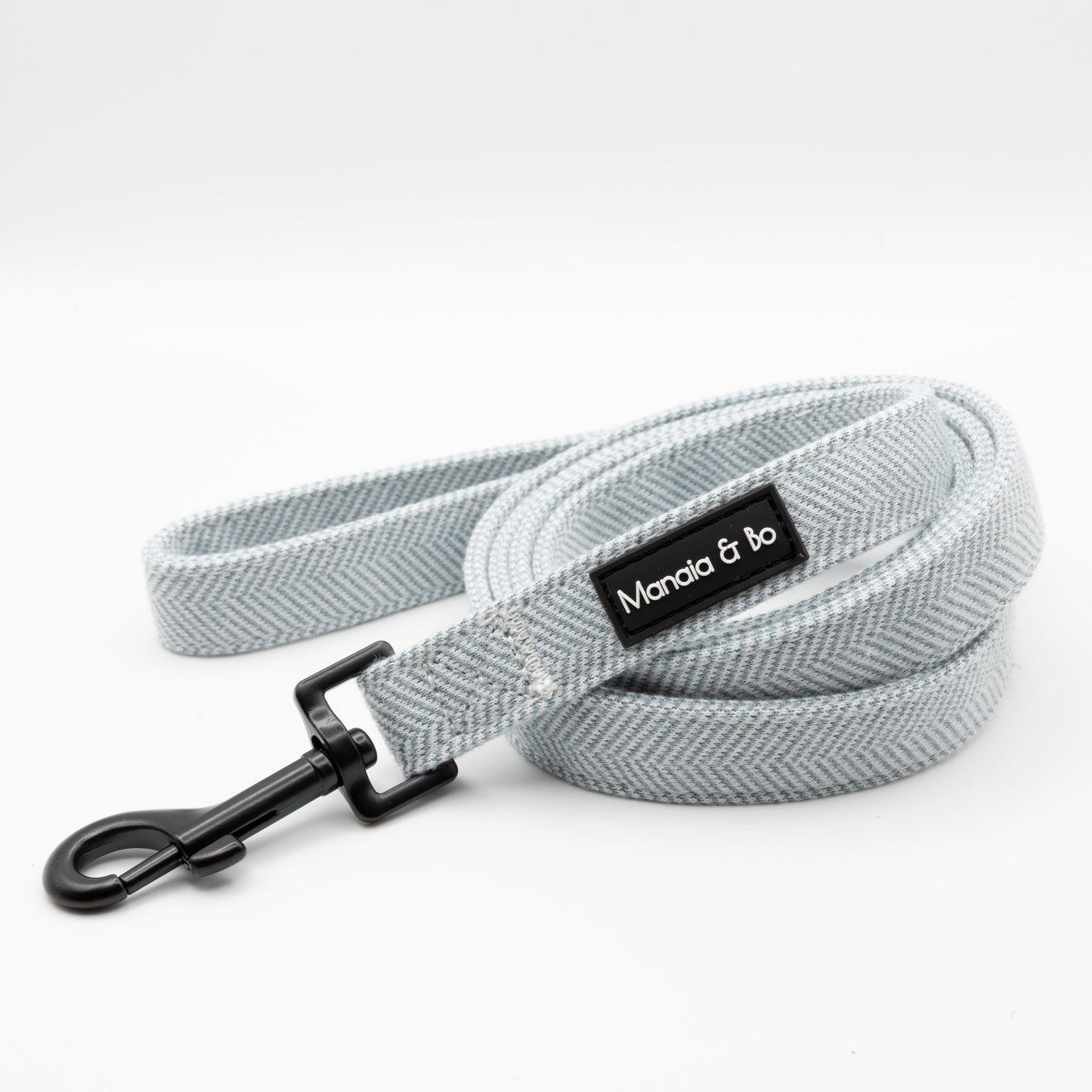The Sky Tweed Dog Lead features a light gray herringbone pattern, black metal clasp, and a Manala & bo label. Stylish and durable, it’s perfect for daily walks.