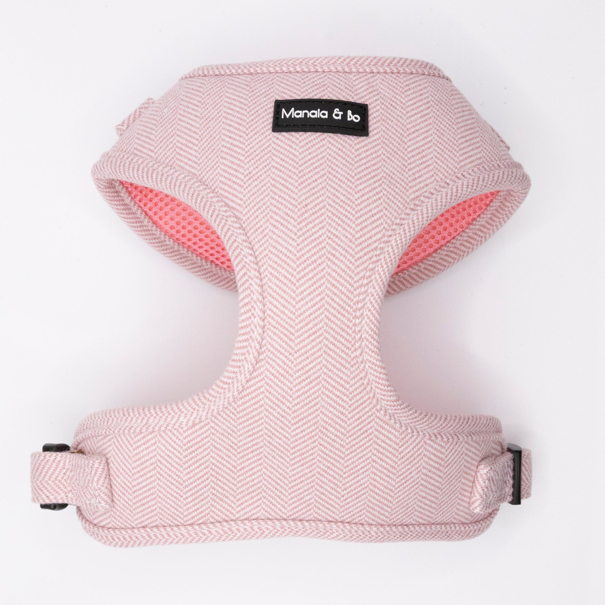The Tea Rose Tweed Dog Harness features a soft, light pink herringbone pattern and "Manala & bo" label on the front. Adjustable for comfort, it's displayed flat against a white background.