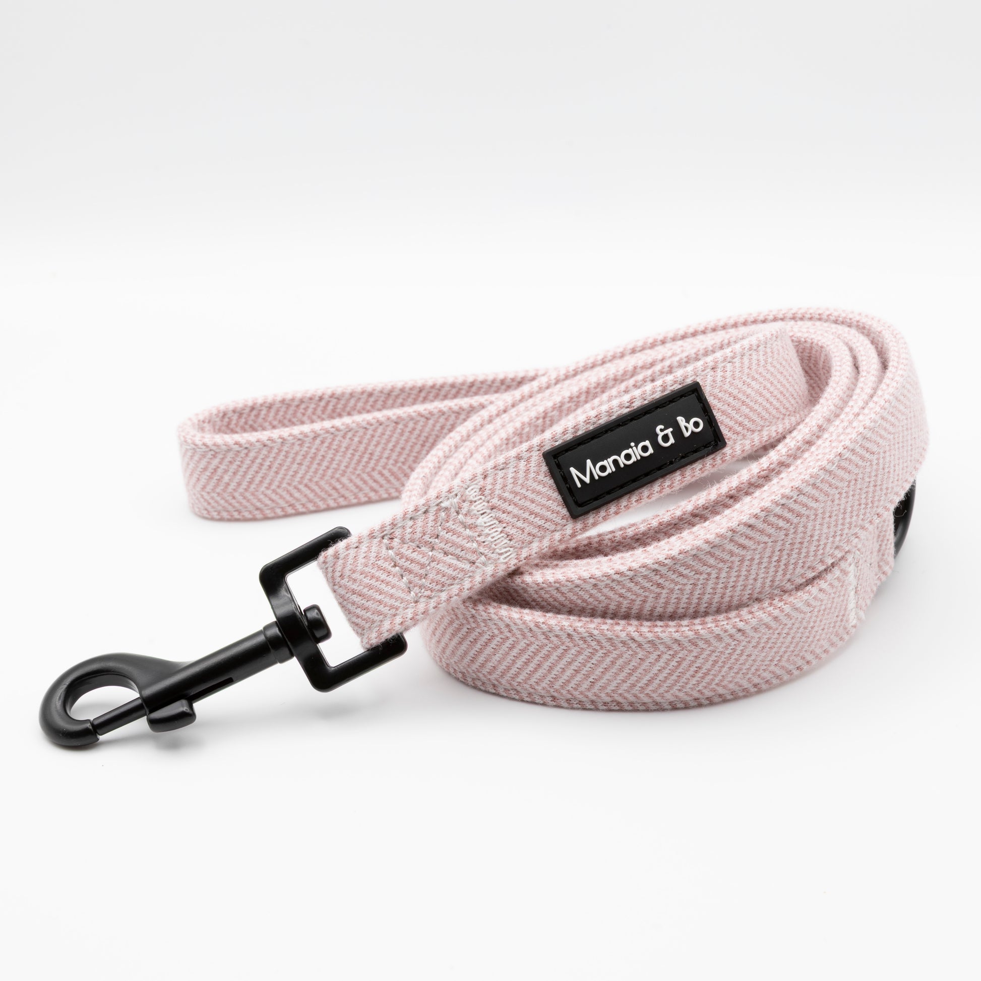 The Tea Rose Tweed Dog Lead features a light pink herringbone pattern, a black metal clasp, and a black Mandia & Bo label on a white background.