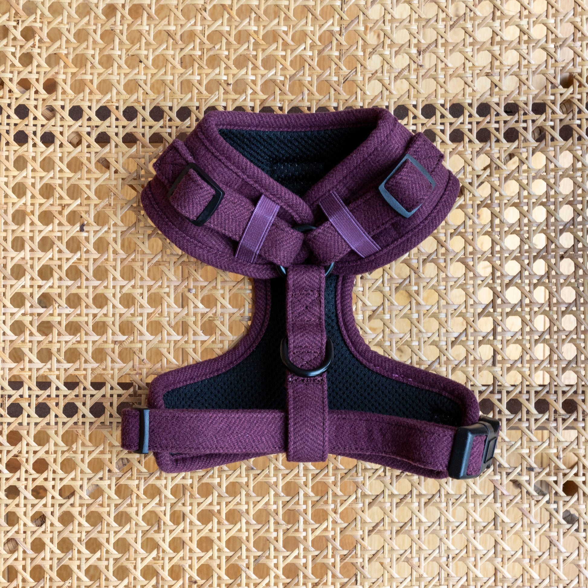 The rear of a Wild Plum tweed Dog Harness, with adjustable straps and a black mesh lining made of quality pet materials, is shown on a woven rattan background.