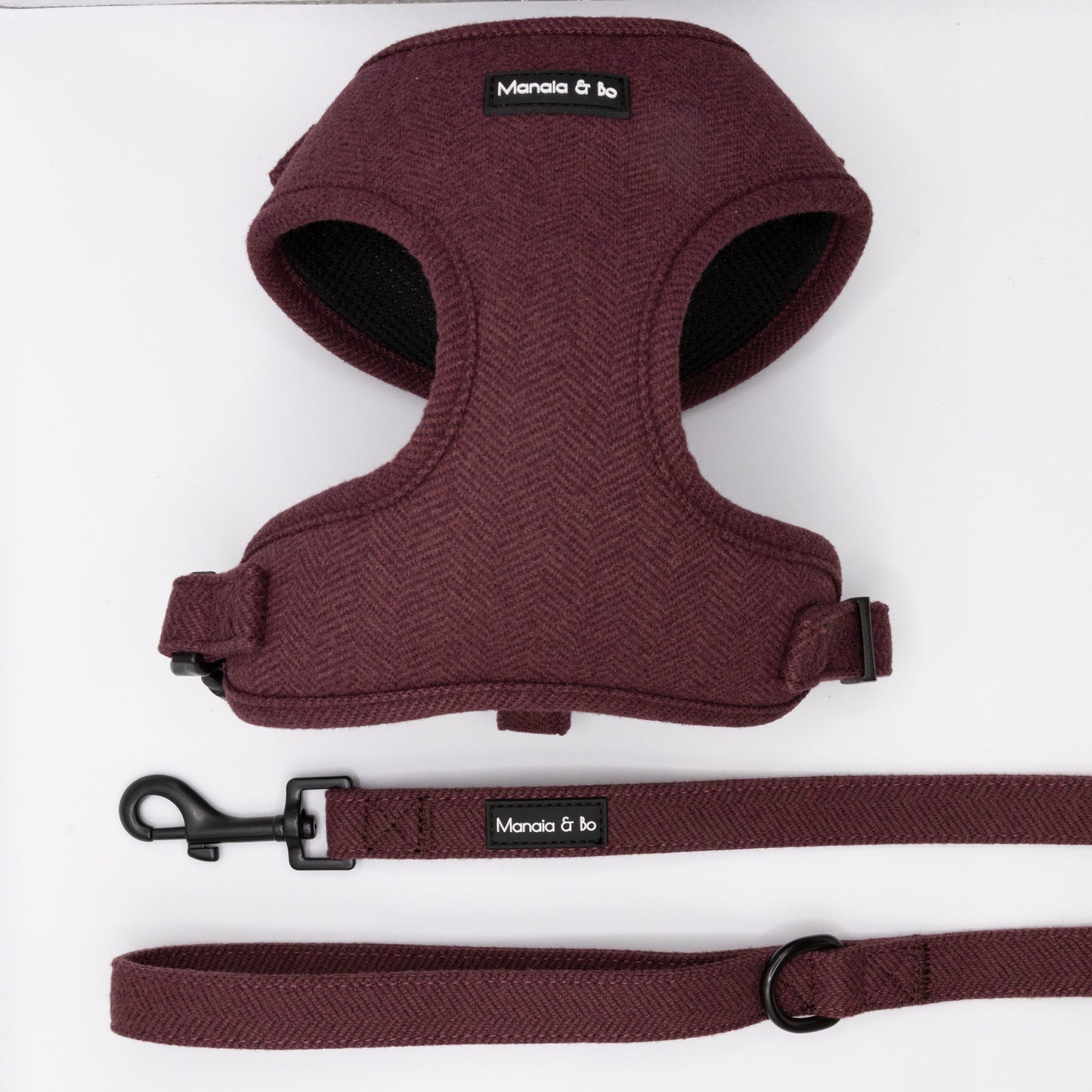 The Wild Plum Tweed Harness & Lead is a maroon herringbone set with black buckles, Manola & Bo labels, plus a matching adjustable harness for small to medium dogs. The leash includes a metal clip and D-ring.